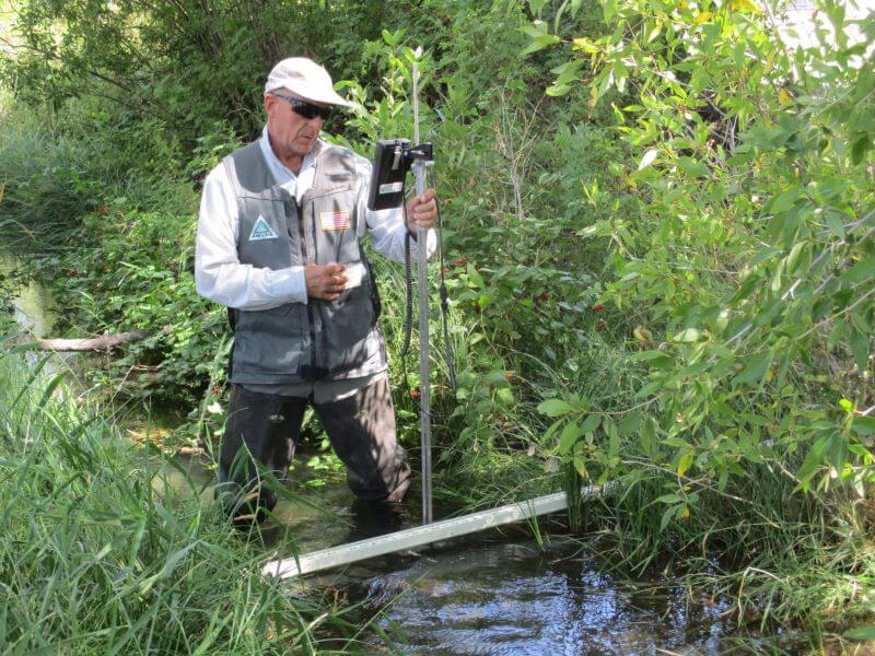 A BBS worker doing a natural resource consultation of wildland hydrology with a measurement tool in the river.